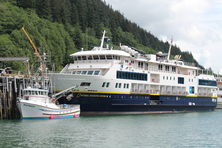 A ferry and fishing boat docked in Skagway, Alaska surrounded by lush greenery.