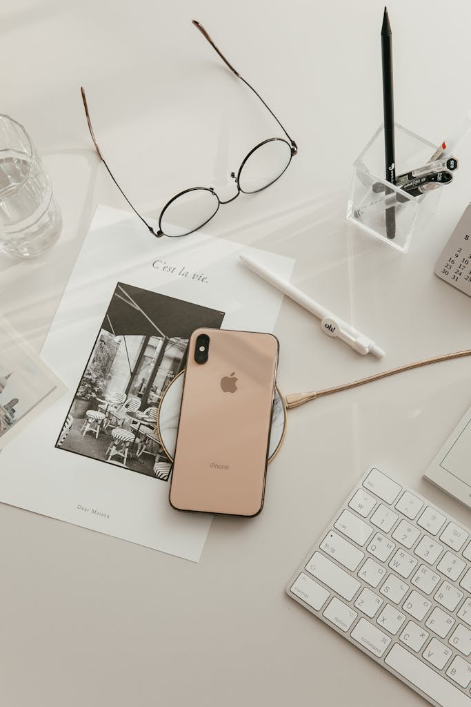 Modern minimalist workspace setup featuring smartphone, keyboard, glasses, and stationery.
