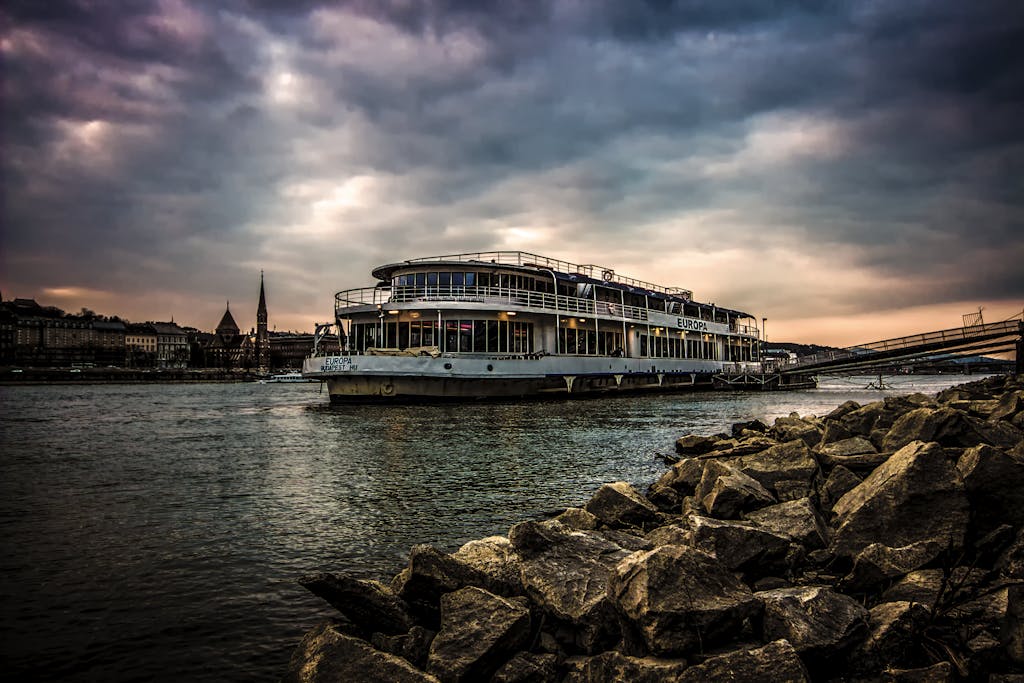 Luxurious river cruise ship sailing on the Danube in Budapest under a dramatic cloudy evening sky.