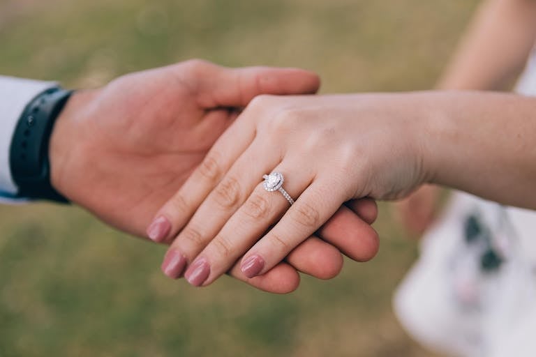 Romantic gesture of couple holding hands, showcasing a diamond engagement ring.