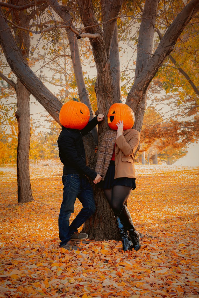 Couple with pumpkin heads enjoying a whimsical moment in a fall park setting.