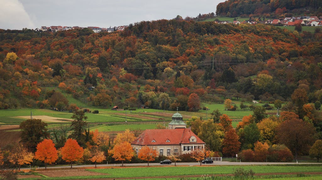 Idyllic fall scenery with a red-roof house amidst colorful foliage and hills.