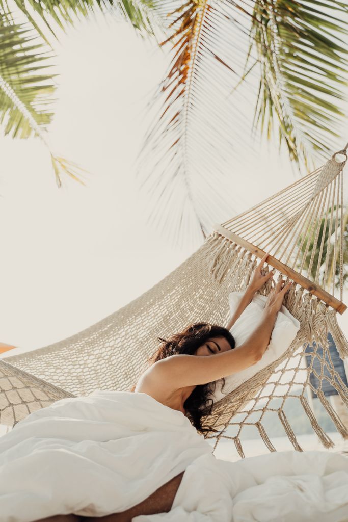 A serene moment of relaxation as a woman enjoys the breeze in a hammock under palm trees.